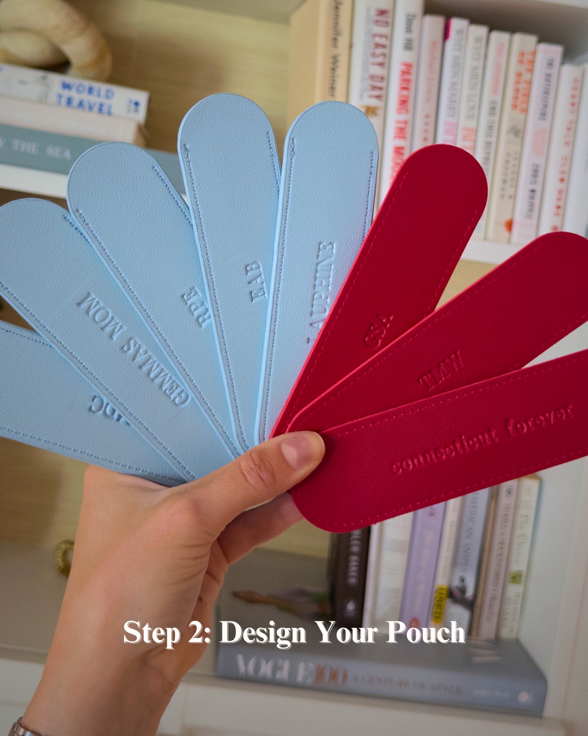 A hand holds a fanned-out set of pouch sample tabs in light blue and red shades, with embossed text including 'IRON SWAN', 'BLUE', 'EAGLE', and 'connections forever'. The background shows a bookshelf with books, and the text overlay reads 'Step 2: Design Your Pouch'.
